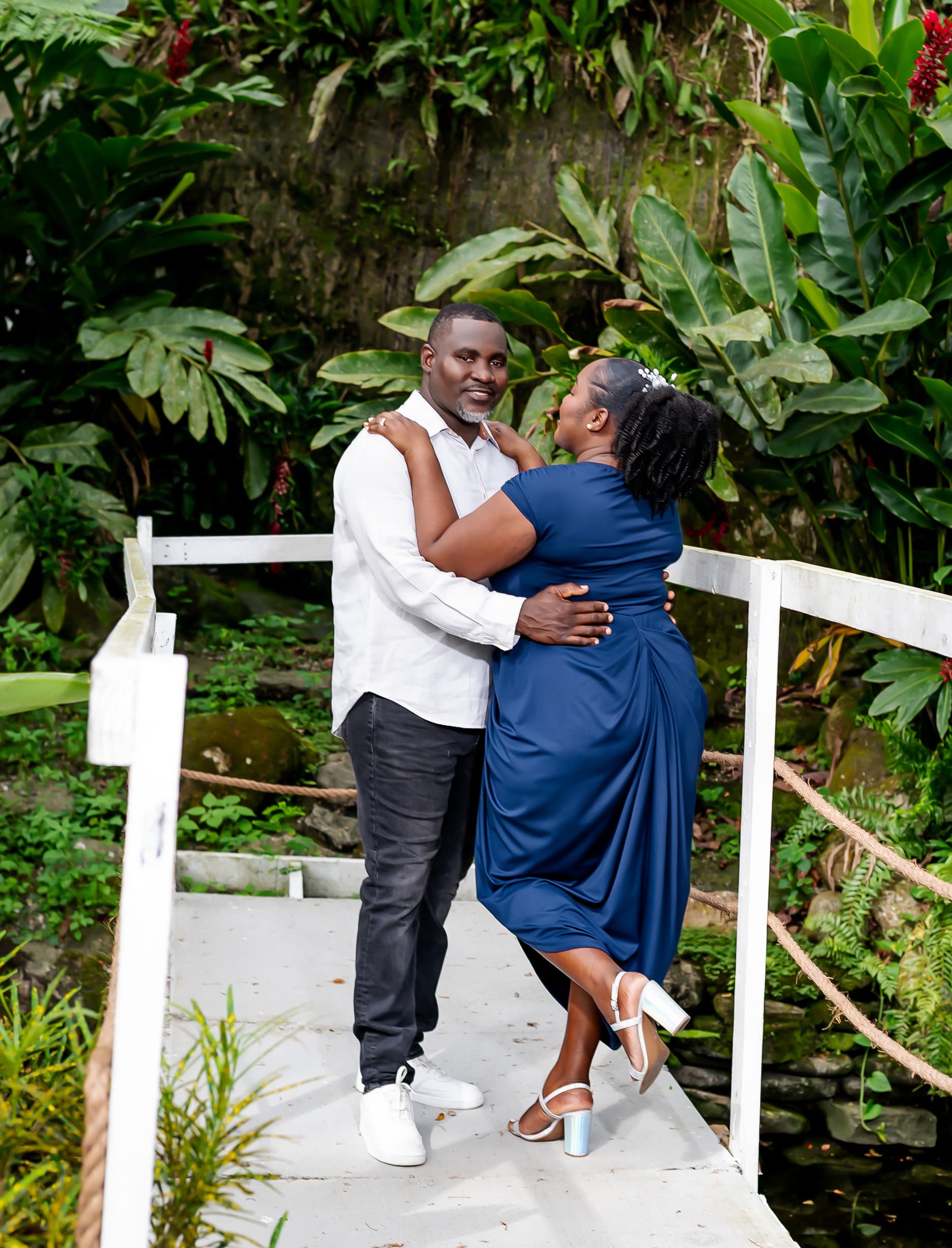 Kerry-Ann and Renado embracing on the bridge surrounded by heliconias